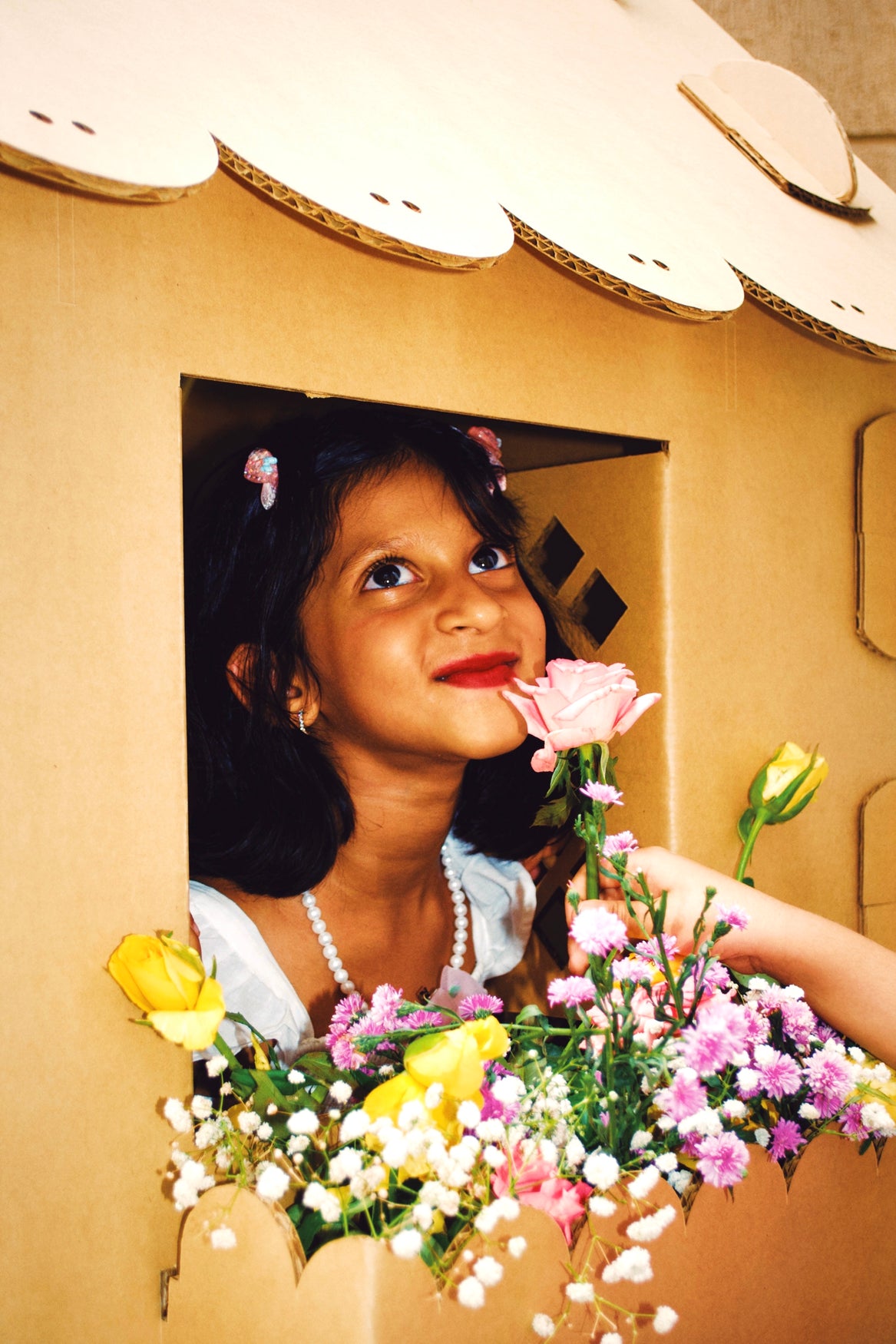 child smiling from a life size playhouse window surrounded by fresh flowers,Child At Flower Pot Playhouse Window,Play Ideas / Gallery,