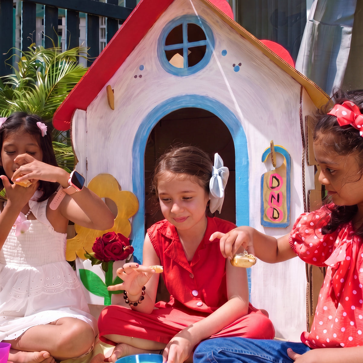 Children having a picnic outside a DUDUK Cubby House with a painted red roof