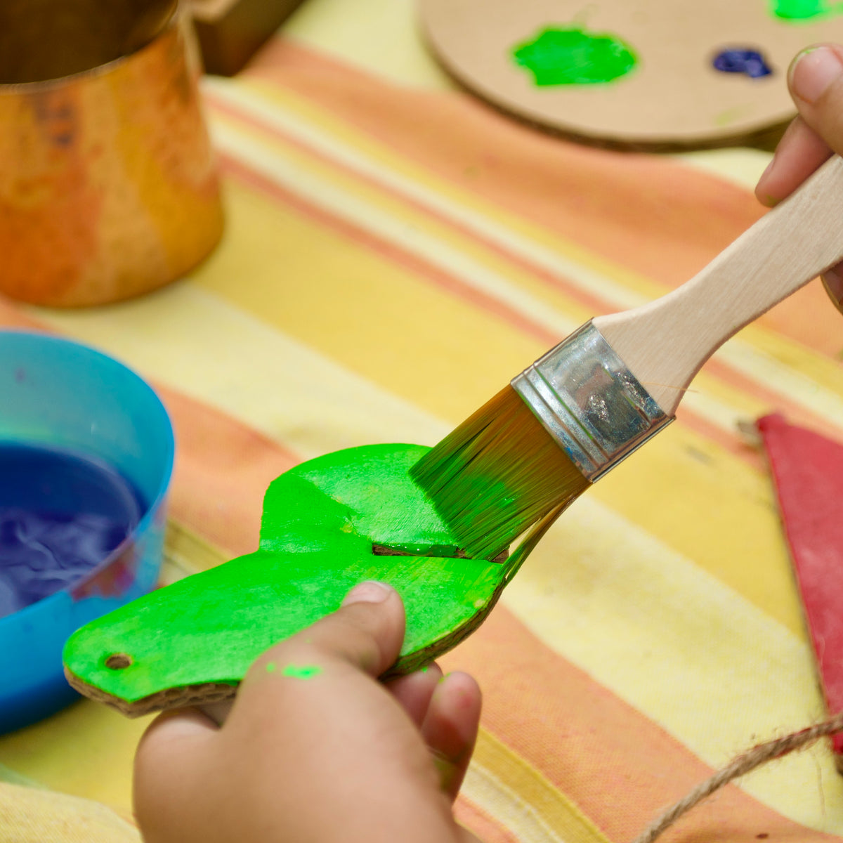 Brush painting a green leaf cut-out for a DUDUK Cubby House
