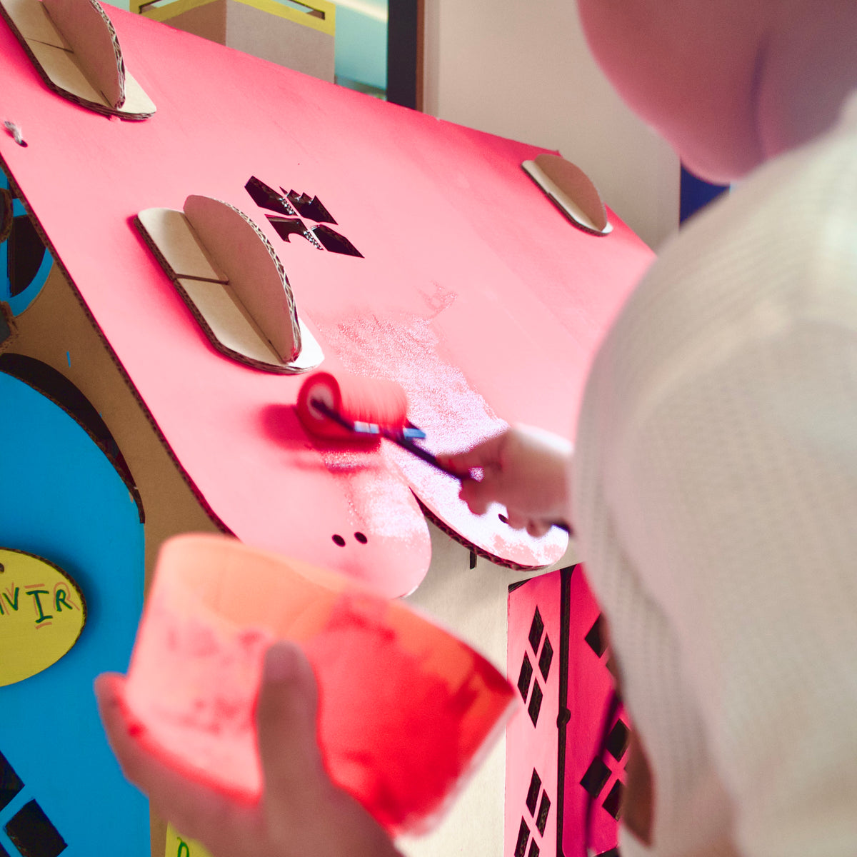 Child rolling pink paint onto the roof of a DUDUK Cubby House